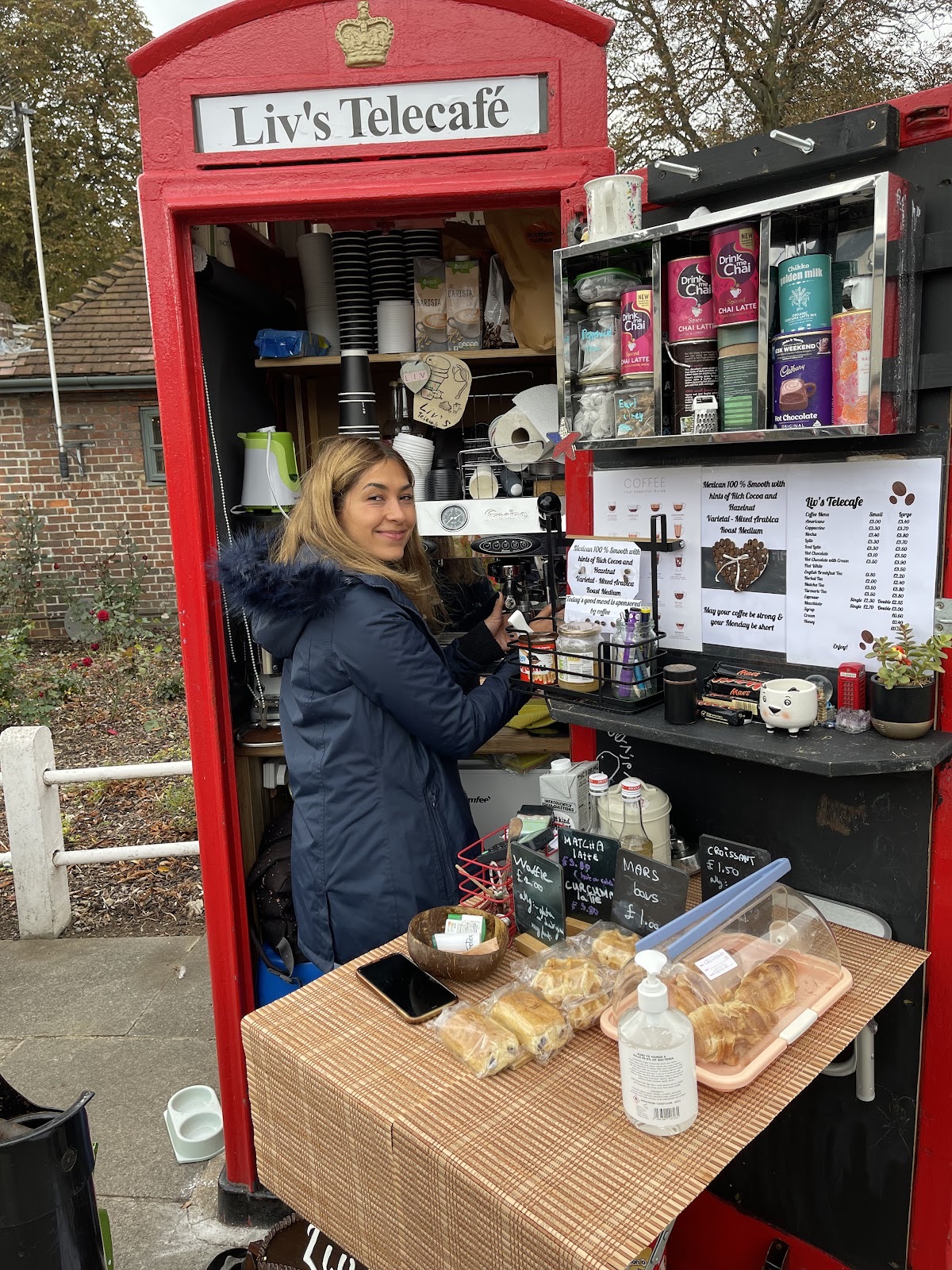 A staff member working inside the kiosk with pastries laid out on the wooden counter