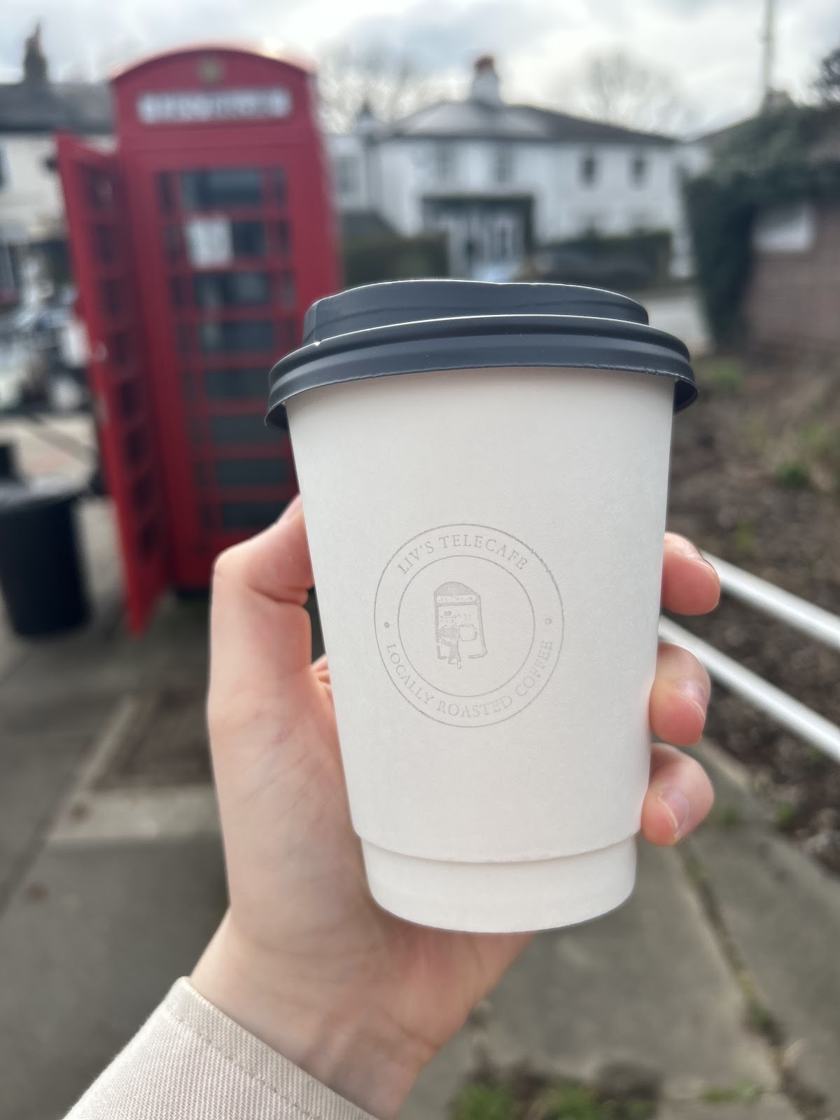 A white takeaway cup held in front of the red phone box