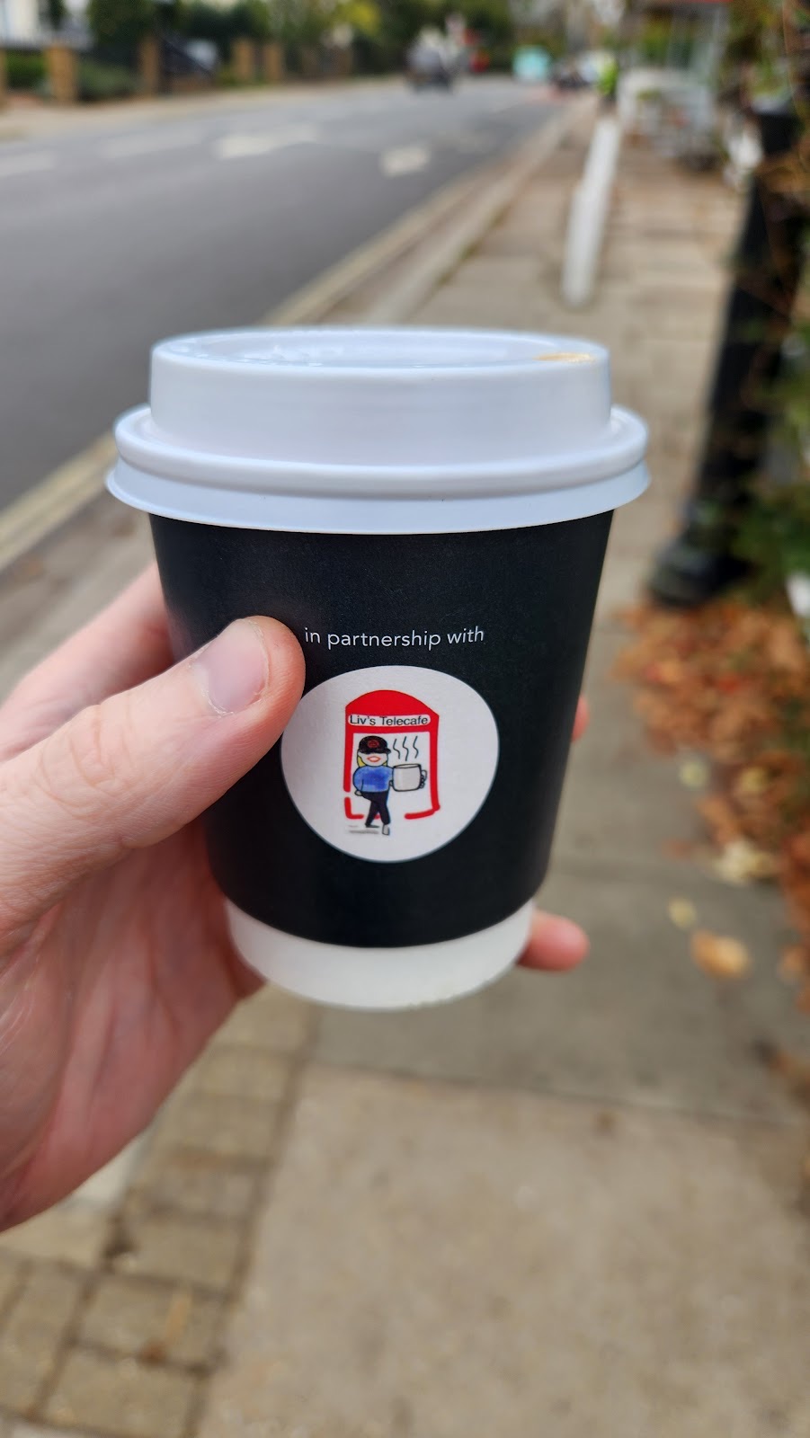A black takeaway coffee cup held on the pavement