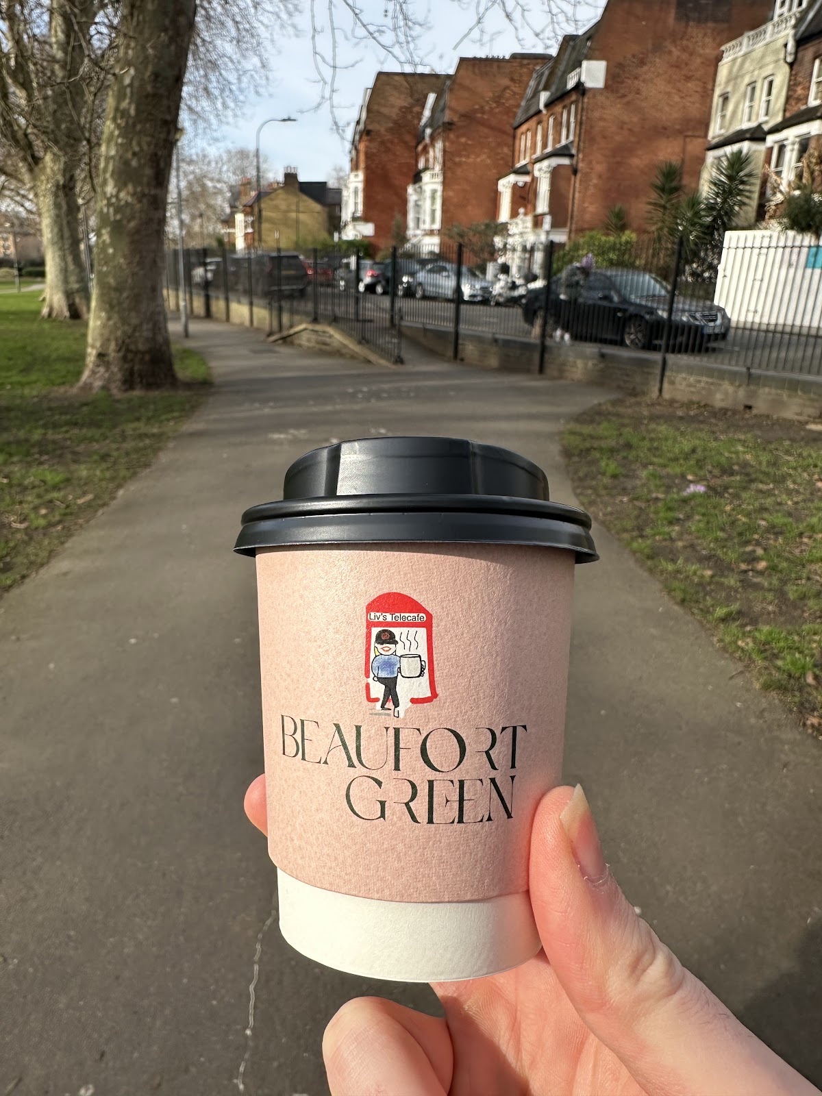 A pink takeaway cup held on a tree-lined park path